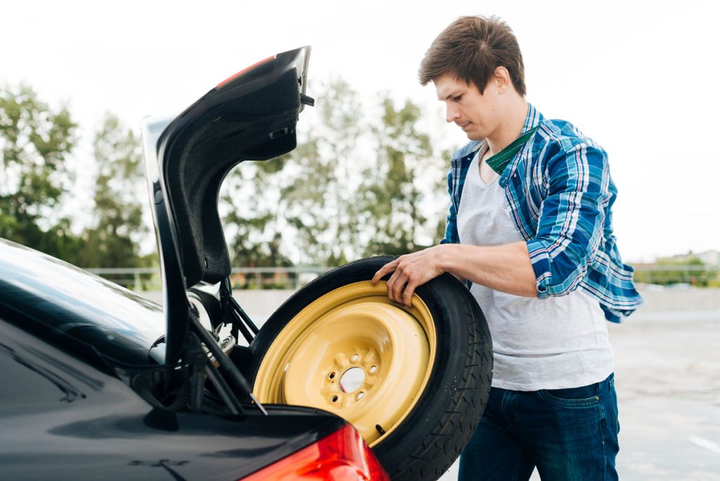 Čovek proverava rezervni točak u svom automobilu, kao deo obavezne opreme.