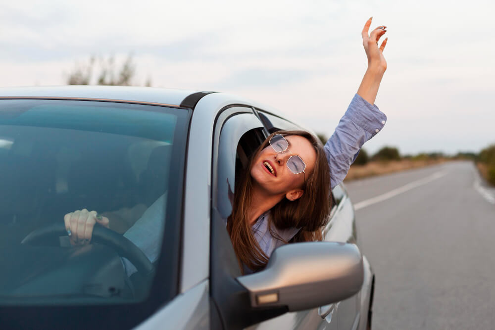 Žena uživa u vožnji automobila.