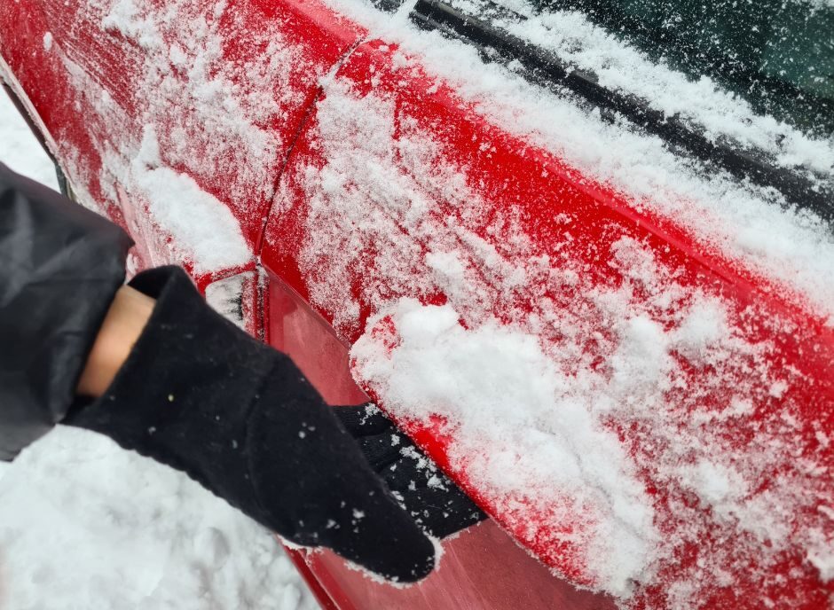 Vozač pokušava da otvori vrata automobila koja su smrznuta tokom hladnog zimskog jutra.